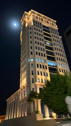 a very tall building lit up at night with the moon in the sky behind it