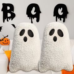 two stuffed ghost pillows sitting on top of a white couch in front of halloween decorations