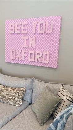 there is a pink sign on the wall above a gray couch with pillows and throw pillows