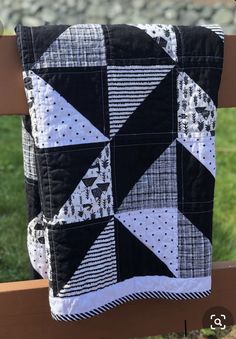 a black and white patchwork quilted pillow on a wooden bench with grass in the background