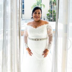 a woman standing in front of a window wearing a white dress and holding her hands on her hips