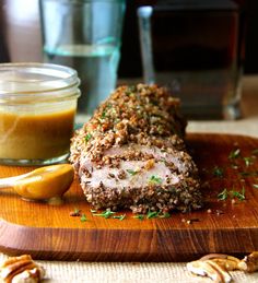 a wooden cutting board topped with meat covered in seasoning next to a jar of mustard