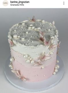 a pink and white cake with butterflies on it's top is decorated with pearls