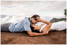 a man and woman laying on top of a mountain kissing while holding each other's forehead