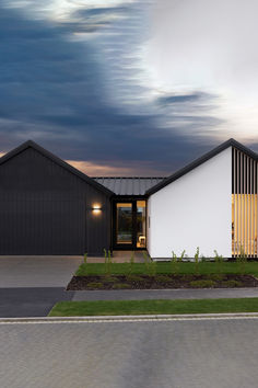 a modern house with black and white architecture on the front lawn at dusk, under a cloudy sky