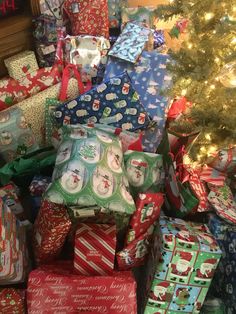 a pile of wrapped presents next to a christmas tree