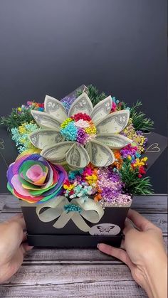 a person is holding a flower arrangement made out of dollar bills and paper machs