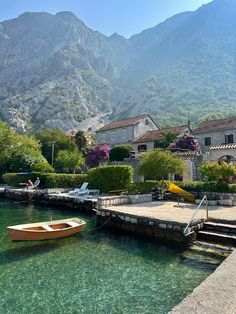 there is a boat that is sitting on the water near some houses and mountains in the background