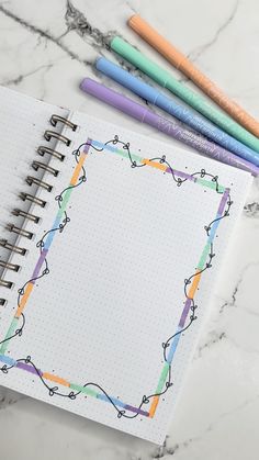 an open spiral notebook with colored pencils and markers next to it on a marble surface