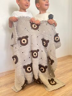 two young boys holding up a crocheted teddy bear blanket