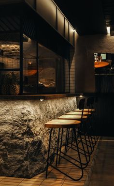 a row of bar stools in front of a stone wall at night with lights on