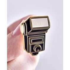 a small black and white camera pin in someone's hand, with the light shining on it