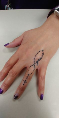 a woman's hand with a cross tattoo on her left wrist and purple nail polish