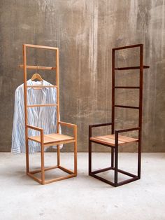 two wooden chairs sitting next to each other in front of a wall with a shirt on it