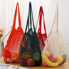 three mesh bags filled with fruit sitting on top of a wooden table next to flowers