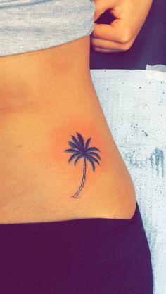 a small palm tree tattoo on the side of a woman's stomach is shown