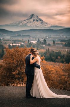 a bride and groom standing on top of a hill with a mountain in the background