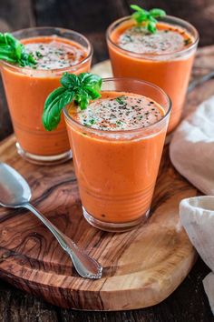 two glasses filled with carrot smoothie and garnished with basil on a cutting board