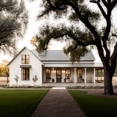 a white house sitting on top of a lush green field next to a large tree