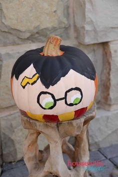 a painted pumpkin sitting on top of a piece of wood next to a stone wall