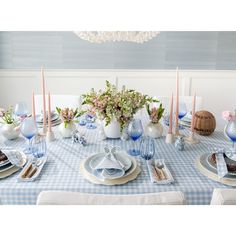 a blue and white table setting with flowers in vases on the centerpiece, plates and utensils