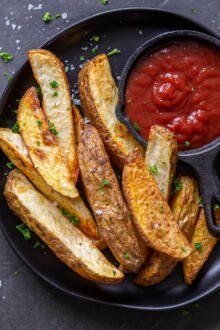 french fries and ketchup on a black plate with a bowl of dipping sauce