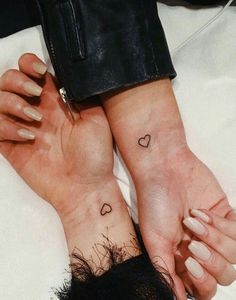 two people holding hands with hearts on their wrist tattooing one another's hand