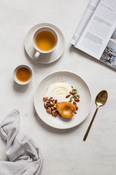 a white plate topped with food next to two cups of tea and an open book