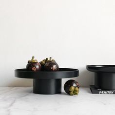 two black trays with fruit on them sitting on a marble counter top next to each other