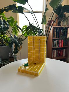 a yellow vase sitting on top of a white table next to a green potted plant