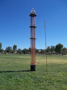 a tall metal pole sitting in the middle of a grass field next to a tree