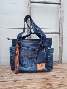 a denim bag sitting on top of a wooden table next to an old ladder with a leather tassel hanging from it