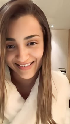 a woman with long hair wearing a white coat and smiling at the camera while taking a selfie