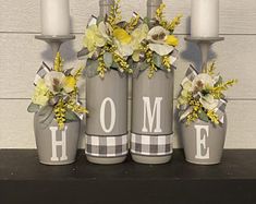 three gray vases with flowers and the word home are sitting on a mantel