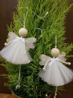 two angel ornaments sitting on top of a potted plant next to a christmas tree