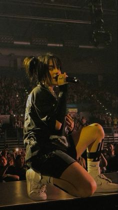 a woman sitting on top of a stage while holding a microphone in her hand and looking at the crowd