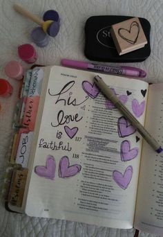 an open bible with purple hearts on it next to markers, pens and pencils