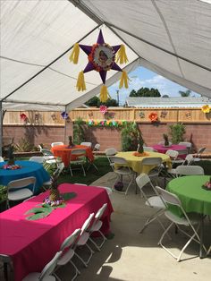 tables and chairs are set up under a tent for an outdoor party with decorations hanging from the ceiling