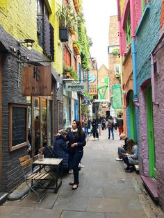 two women sitting on a bench in an alleyway with people walking by and buildings painted multicolored