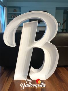 the letter b is white in color and sits on a wooden floor