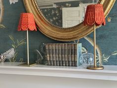 two lamps are on top of a mantle with books and a mirror in the background