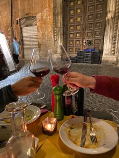 two people toasting wine glasses at a table with food and drinks in front of them