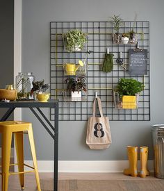 a table with two yellow stools next to a wall mounted planter and potted plants