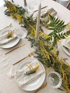 the table is set with white plates and yellow flowers, candles, and napkins