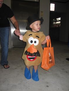 a little boy dressed up as mr potato head holding an orange bag and wearing blue rubber boots