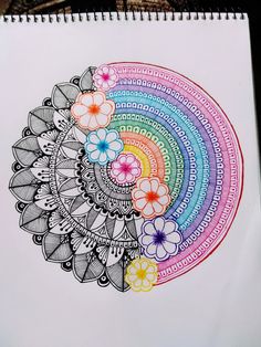 a drawing on paper with flowers in the center and rainbow colors around it, sitting on top of a table