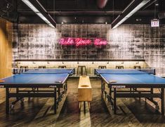 ping pong tables are lined up in the middle of a room with neon signs on the wall