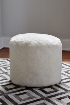 a round white ottoman sitting on top of a black and white rug