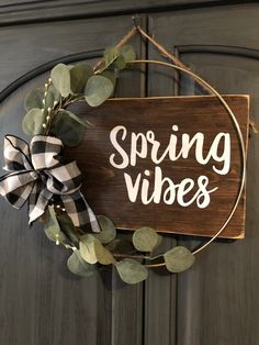 a wooden sign that says spring vibes hanging on a door with greenery around it