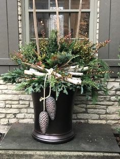 a potted plant with pine cones and greenery in front of a brick building